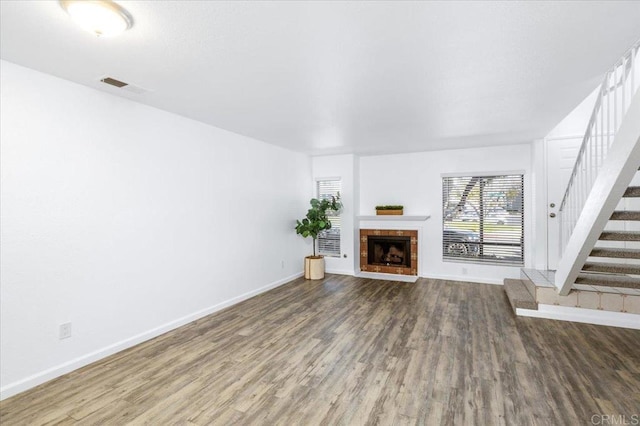 unfurnished living room with a tile fireplace, wood finished floors, visible vents, and stairs