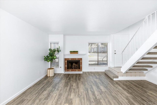 unfurnished living room featuring stairway, baseboards, wood finished floors, and a tile fireplace