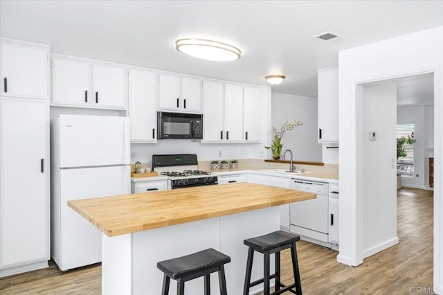 kitchen featuring white appliances, visible vents, a breakfast bar, light wood-style floors, and a sink