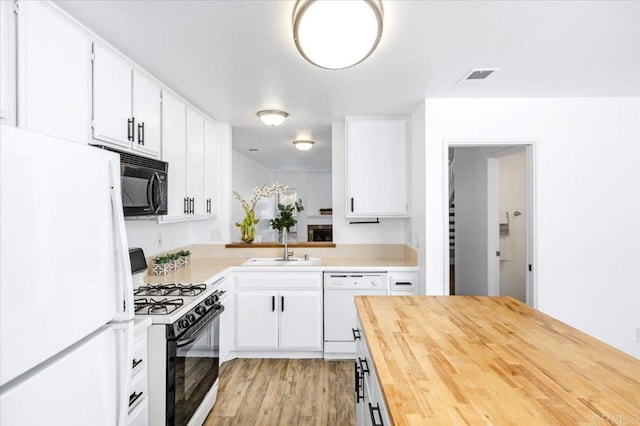 kitchen with white appliances, butcher block counters, white cabinets, and a sink