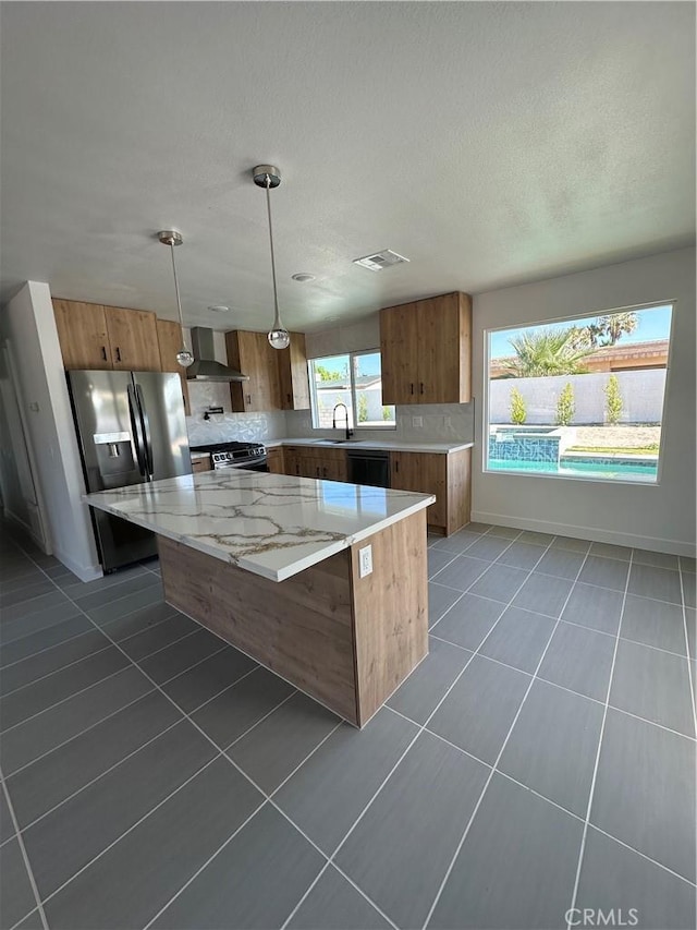 kitchen featuring sink, wall chimney range hood, appliances with stainless steel finishes, hanging light fixtures, and a center island