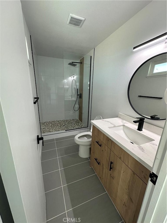 bathroom with tile patterned flooring, vanity, tiled shower, and toilet