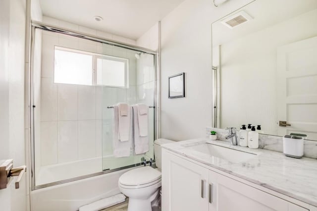 full bathroom with enclosed tub / shower combo, vanity, and toilet