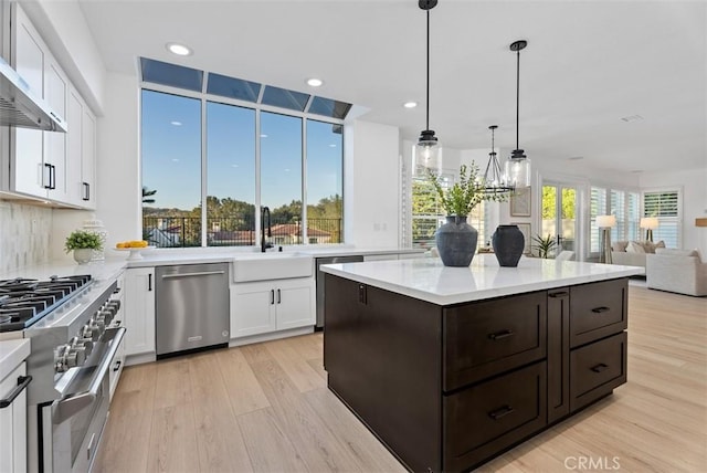 kitchen with appliances with stainless steel finishes, pendant lighting, sink, white cabinets, and light hardwood / wood-style flooring