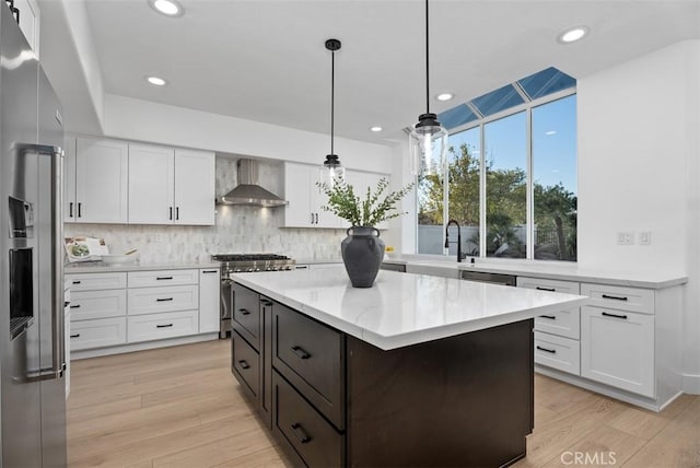 kitchen with hanging light fixtures, a kitchen island, wall chimney range hood, and white cabinets