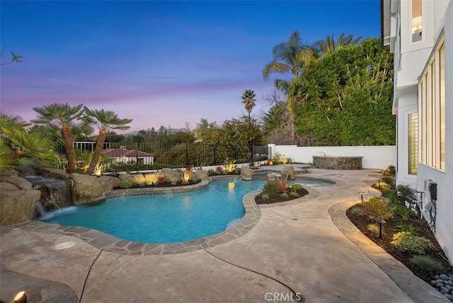 pool at dusk with pool water feature and a patio