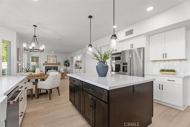 kitchen with light hardwood / wood-style flooring, appliances with stainless steel finishes, white cabinetry, hanging light fixtures, and dark brown cabinets