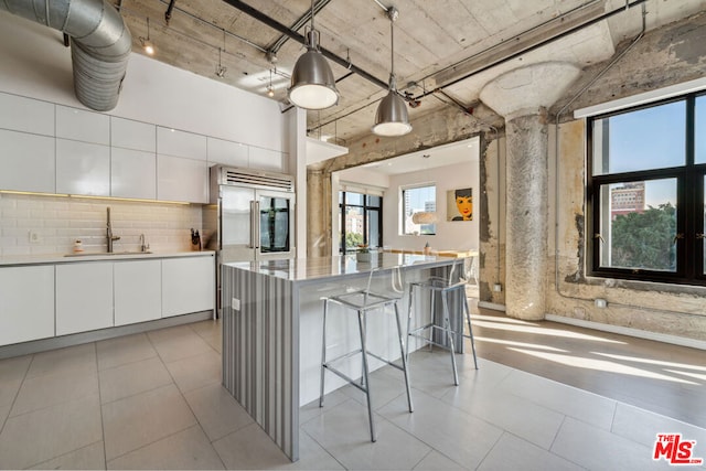 kitchen featuring sink, tasteful backsplash, hanging light fixtures, a kitchen breakfast bar, and white cabinets