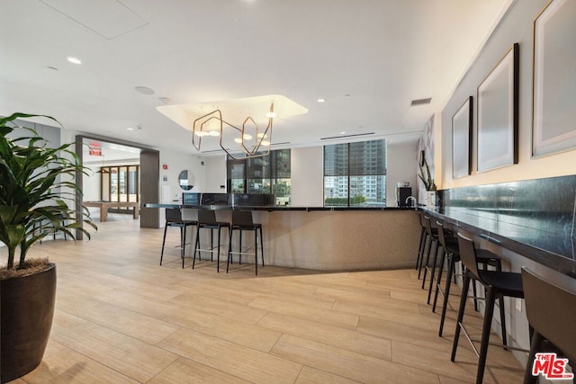 kitchen with light hardwood / wood-style flooring, kitchen peninsula, a chandelier, and a kitchen bar