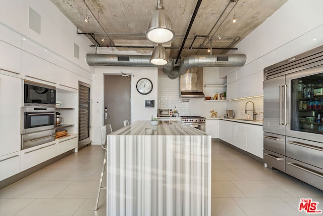 kitchen featuring wall chimney range hood, white cabinetry, stainless steel appliances, a center island, and decorative light fixtures