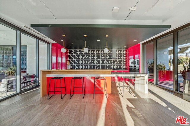 bar with expansive windows, appliances with stainless steel finishes, hardwood / wood-style floors, and wall chimney range hood