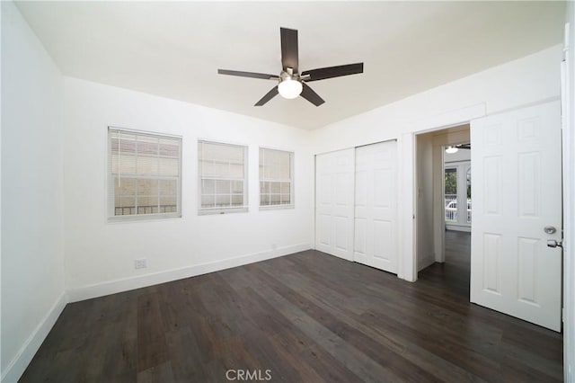 unfurnished bedroom with a closet, baseboards, and dark wood-style flooring