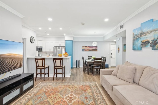 living room with sink, ornamental molding, and light wood-type flooring