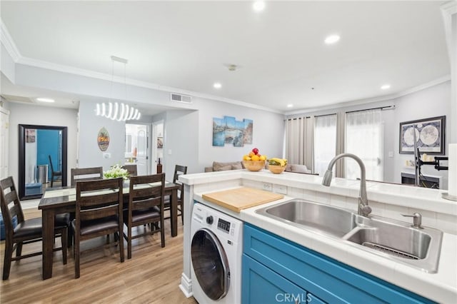 kitchen with blue cabinets, washer / dryer, sink, ornamental molding, and light hardwood / wood-style floors