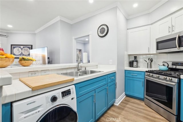 kitchen with appliances with stainless steel finishes, washer / dryer, sink, crown molding, and blue cabinetry