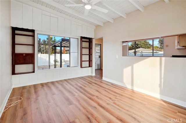 spare room with beamed ceiling, ceiling fan, a healthy amount of sunlight, and light wood-type flooring