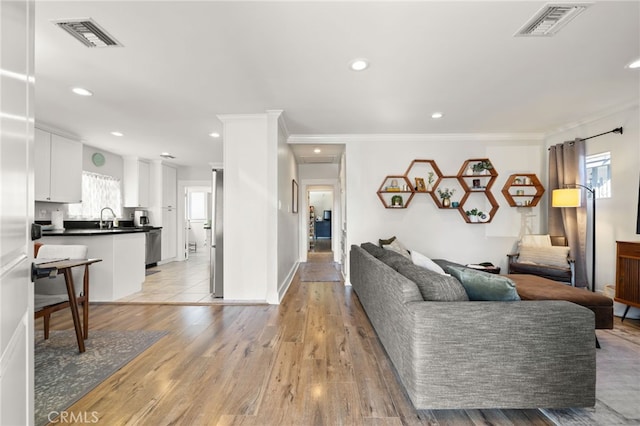 living room featuring crown molding, sink, and light hardwood / wood-style flooring