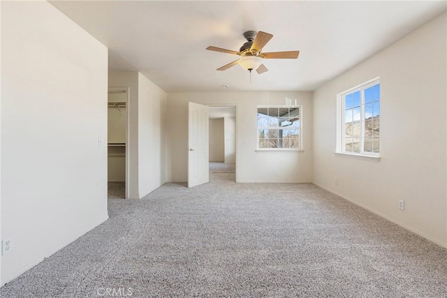 unfurnished bedroom with ceiling fan, light colored carpet, a closet, and a walk in closet