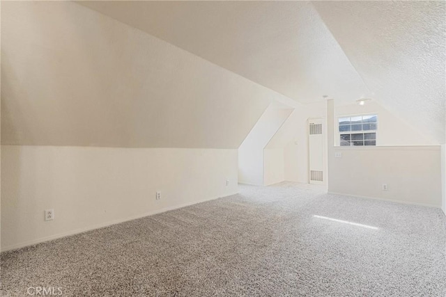 additional living space featuring vaulted ceiling, carpet, and a textured ceiling