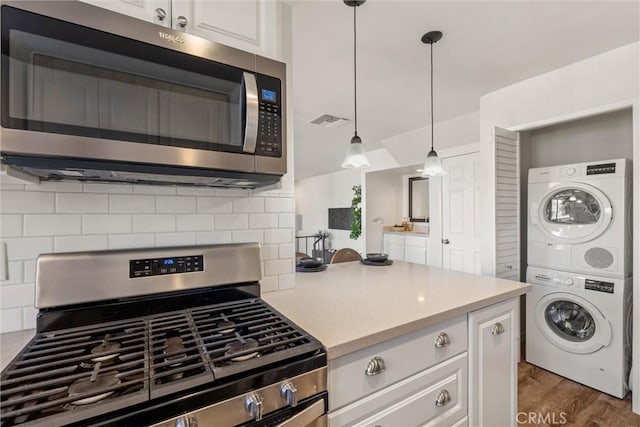 kitchen with pendant lighting, tasteful backsplash, white cabinetry, stacked washer and clothes dryer, and stainless steel appliances