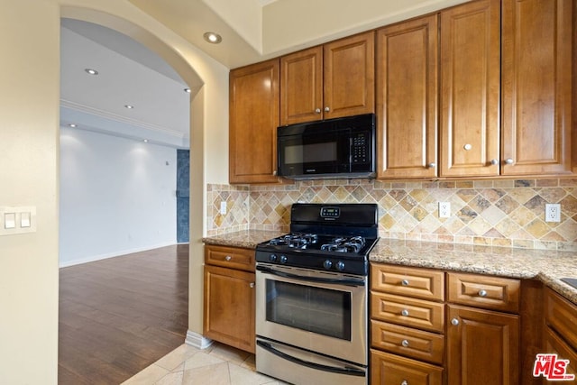 kitchen with light tile patterned flooring, backsplash, crown molding, light stone counters, and gas range