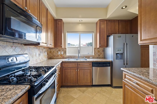 kitchen with light stone counters, sink, decorative backsplash, and appliances with stainless steel finishes