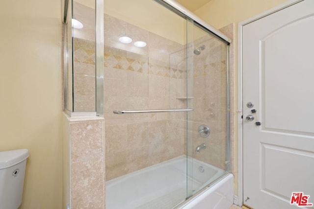 bathroom featuring toilet and bath / shower combo with glass door