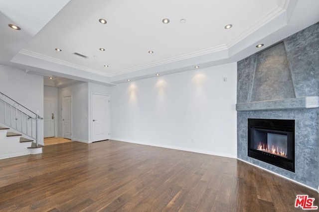 unfurnished living room with a raised ceiling, wood-type flooring, and ornamental molding