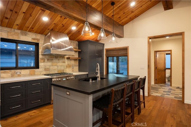 kitchen with sink, a kitchen island with sink, a kitchen breakfast bar, decorative light fixtures, and wall chimney exhaust hood