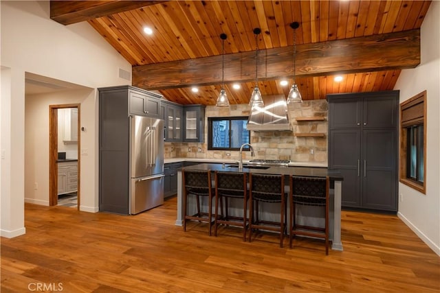 kitchen featuring tasteful backsplash, high end refrigerator, decorative light fixtures, and a kitchen island with sink