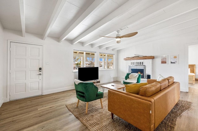 living room featuring a brick fireplace, beam ceiling, ceiling fan, and light wood-type flooring