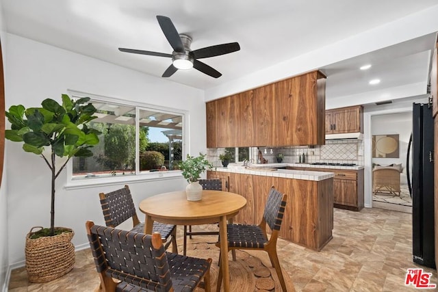 kitchen featuring ceiling fan, tasteful backsplash, black fridge, tile countertops, and kitchen peninsula