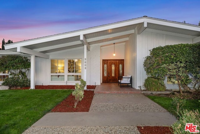 exterior entry at dusk featuring a yard and covered porch