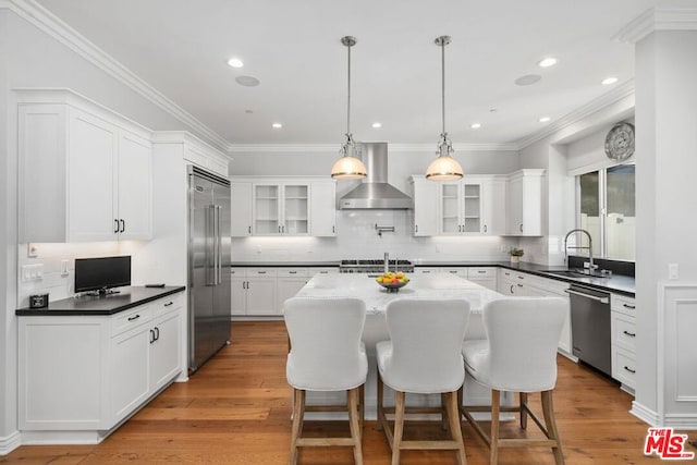 kitchen with wall chimney exhaust hood, stainless steel appliances, a center island, and sink