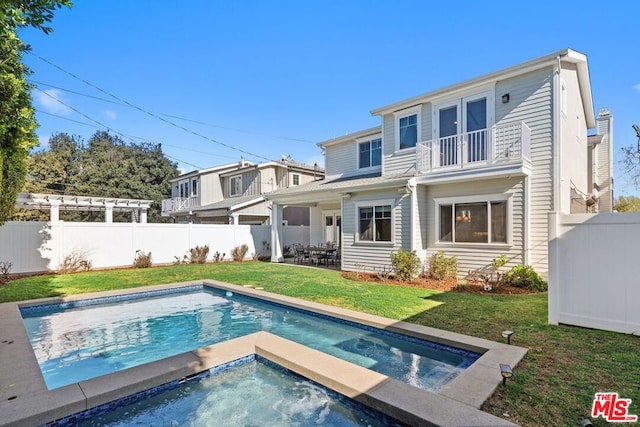 back of property featuring a balcony, a pool with hot tub, and a lawn