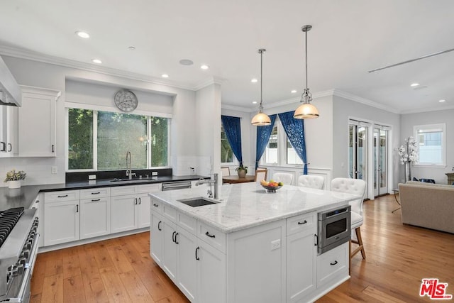 kitchen with white cabinetry, sink, dark stone countertops, stainless steel appliances, and a center island with sink