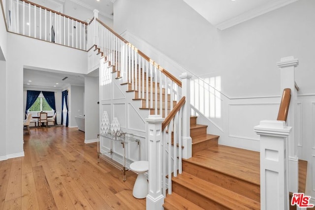 stairs featuring a towering ceiling, ornamental molding, and hardwood / wood-style floors