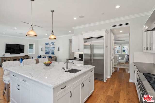 kitchen with high quality appliances, white cabinetry, sink, a breakfast bar area, and a center island with sink