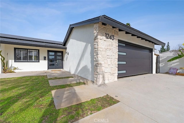 view of front facade featuring a garage, a front yard, french doors, and solar panels