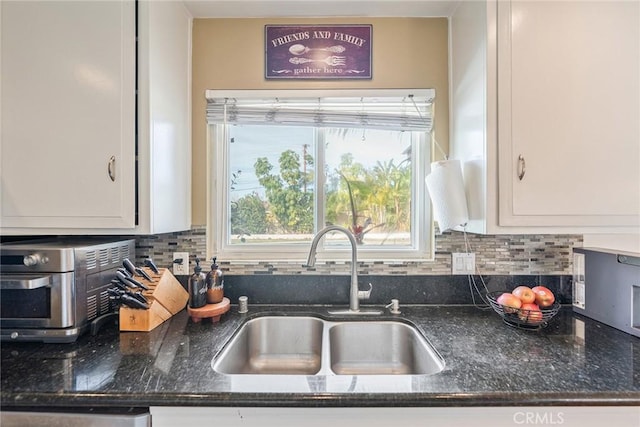 kitchen with tasteful backsplash, sink, dark stone countertops, and white cabinets