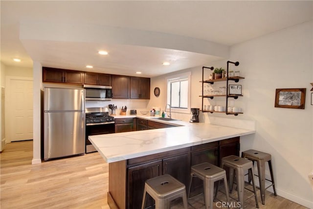 kitchen featuring sink, light hardwood / wood-style flooring, a kitchen breakfast bar, stainless steel appliances, and kitchen peninsula