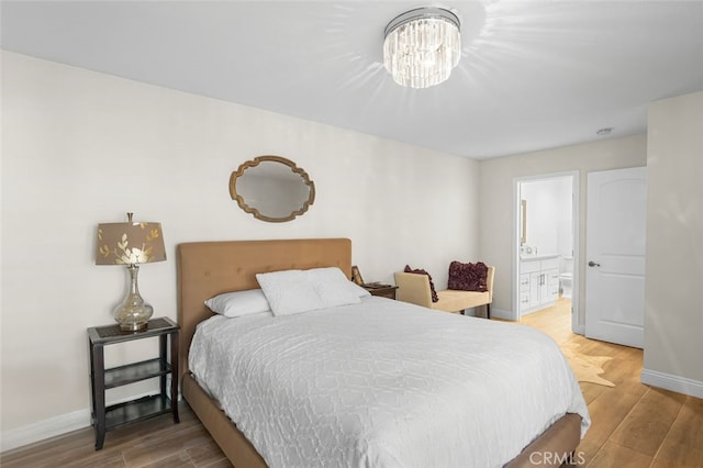 bedroom with an inviting chandelier, ensuite bathroom, and hardwood / wood-style floors