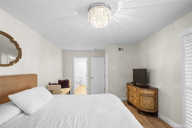 bedroom featuring connected bathroom, an inviting chandelier, and light hardwood / wood-style flooring