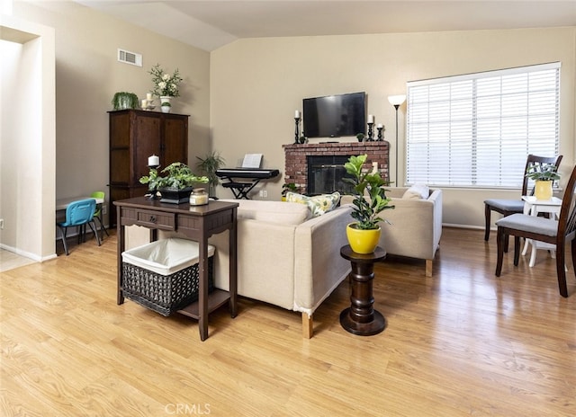 living room with lofted ceiling, a brick fireplace, and light hardwood / wood-style flooring