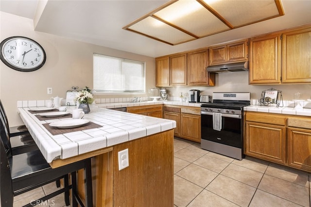 kitchen featuring light tile patterned floors, tile counters, and gas stove