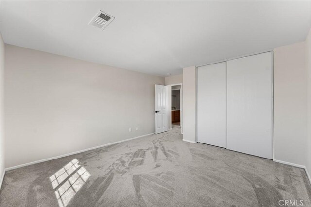 unfurnished bedroom with light colored carpet and a closet