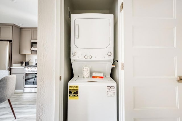 washroom with stacked washer and dryer and light hardwood / wood-style floors