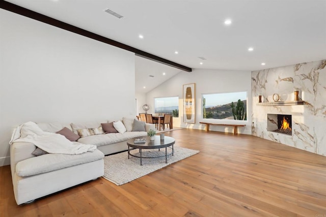 living room with vaulted ceiling with beams, a fireplace, and light hardwood / wood-style floors