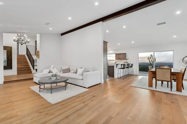 living room featuring an inviting chandelier, beamed ceiling, and light wood-type flooring