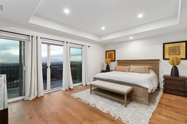 bedroom with wood-type flooring, access to exterior, and a raised ceiling